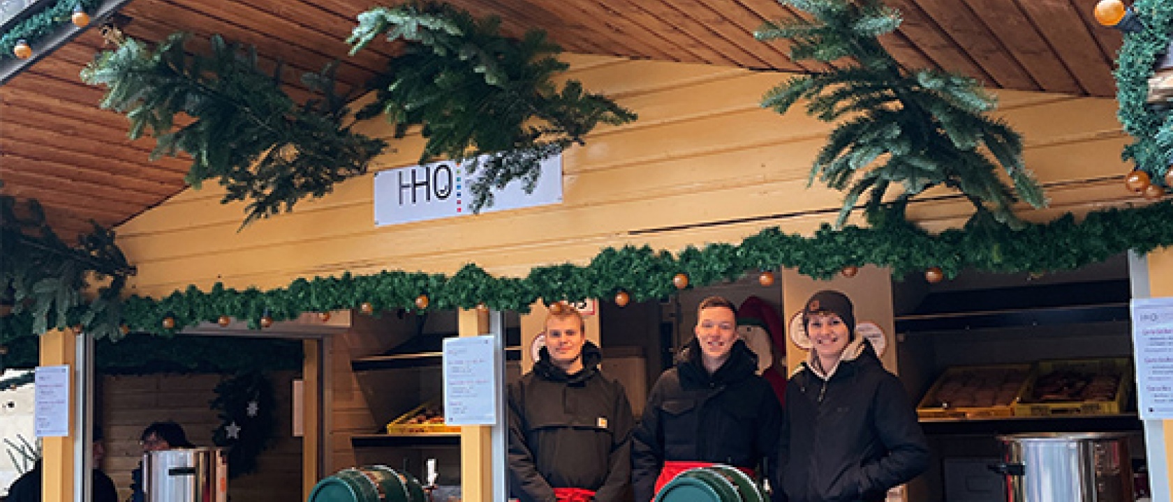 Drei unserer Auszubildenden stehen im Weihnachtsmarkt Stand der HHO